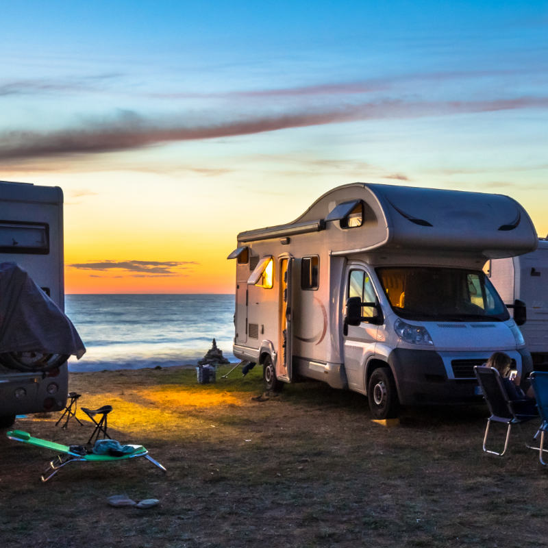 Urlaub mit dem Wohnmobil am Strand im Hintergrund das Meer bei Sonneuntergang