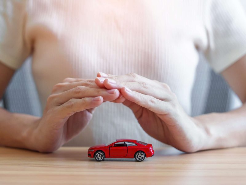Rotes Autospielzeug auf dem Tisch, Hände bilden Schutz über Fahrzeug